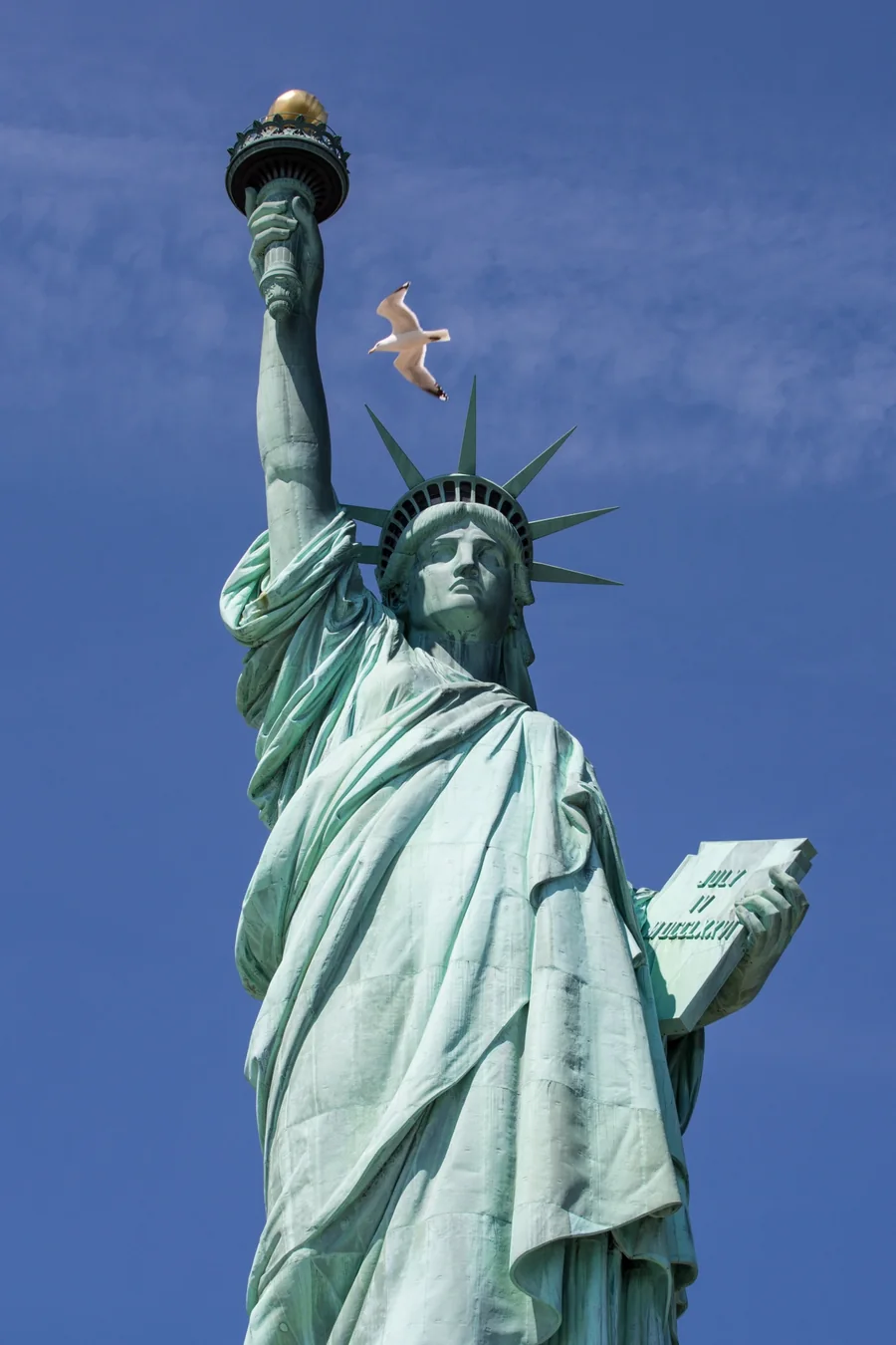 The Statue of Liberty raising her torch against a blue sky